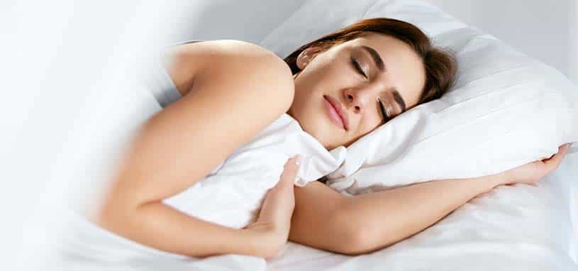 Woman peacefully sleeping on a white pillow and bed with cozy white bedding