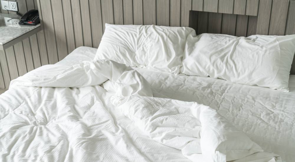 Unmade bed with white pillows and wrinkled white bedding in a modern hotel room