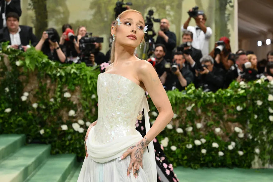 Celebrity in elegant white strapless gown with floral details posing on green carpet at gala event